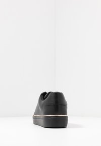 Black leather sneaker with a low profile, textured finish, and rubber sole. Features a stitched seam and subtle contrasting accent on the midsole.