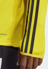 T-shirt de sport jaune à manches longues avec des accents noirs à trois bandes, doté d'un tissu texturé et d'un ajustement serré au poignet.