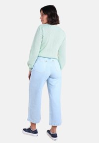 Pull en mailles vert clair, coupe décontractée, associé à un jean taille haute bleu clair. Le mannequin porte des baskets navy. Design minimaliste, sans motifs.