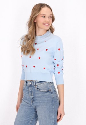 Lichtblauwe gebreide trui met rode hartpatronen, geribde manchetten en zoom; gedragen met hoge blauwe denim jeans.
