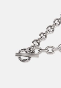 Ezüst fém lánc karkötő nagy szemekkel, amely egy ösztönző csattal rendelkezik, dombornyomott kör alakú részlettel és egy egyenes rudazatú záródással.