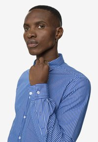 Gestreept blauw overhemd met witte verticale strepen. Heeft een gestructureerde kraag en manchetten, een gladde textuur en een figuurvormig ontwerp.