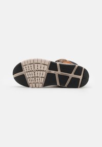 Suela de zapato deportivo negra y beige con un patrón texturizado. Presenta material de goma y surcos de tracción distintivos para agarre y estabilidad.