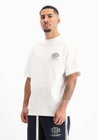 Witte katoenen t-shirt met ronde hals en korte mouwen. Bevat een grafisch logo op de linkerborst. Glad textuur, ontspannen pasvorm.