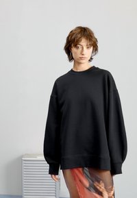 Sudadera negra de gran tamaño con cuello redondo y hombros caídos, hecha de un tejido suave. Combinada con una falda fluida y estampada.
