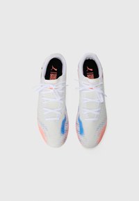 Une paire de chaussures de sport blanches avec des accents bleus et oranges et des lacets blancs, vues d'en haut sur un fond blanc uni.