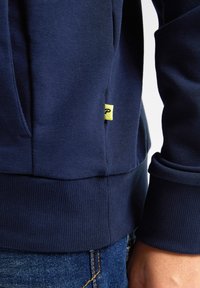 Felpa blu navy realizzata in tessuto misto cotone con polsini e orlo a costine. Presenta un piccolo'etichetta gialla del marchio sul lato sinistro della cucitura.