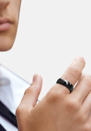 Svart keramikkring med en glat, blank overflate, båret på en finger, som viser et enkelt bånddesign mot en nøytral bakgrunn.