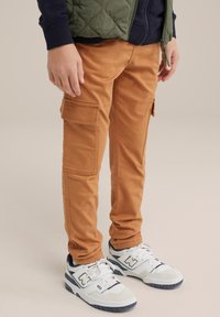 Roestkleurige cargo-broeken met zijzakken en een slim fit, gecombineerd met witte sneakers met marineblauwe accenten en een textuurmateriaal.