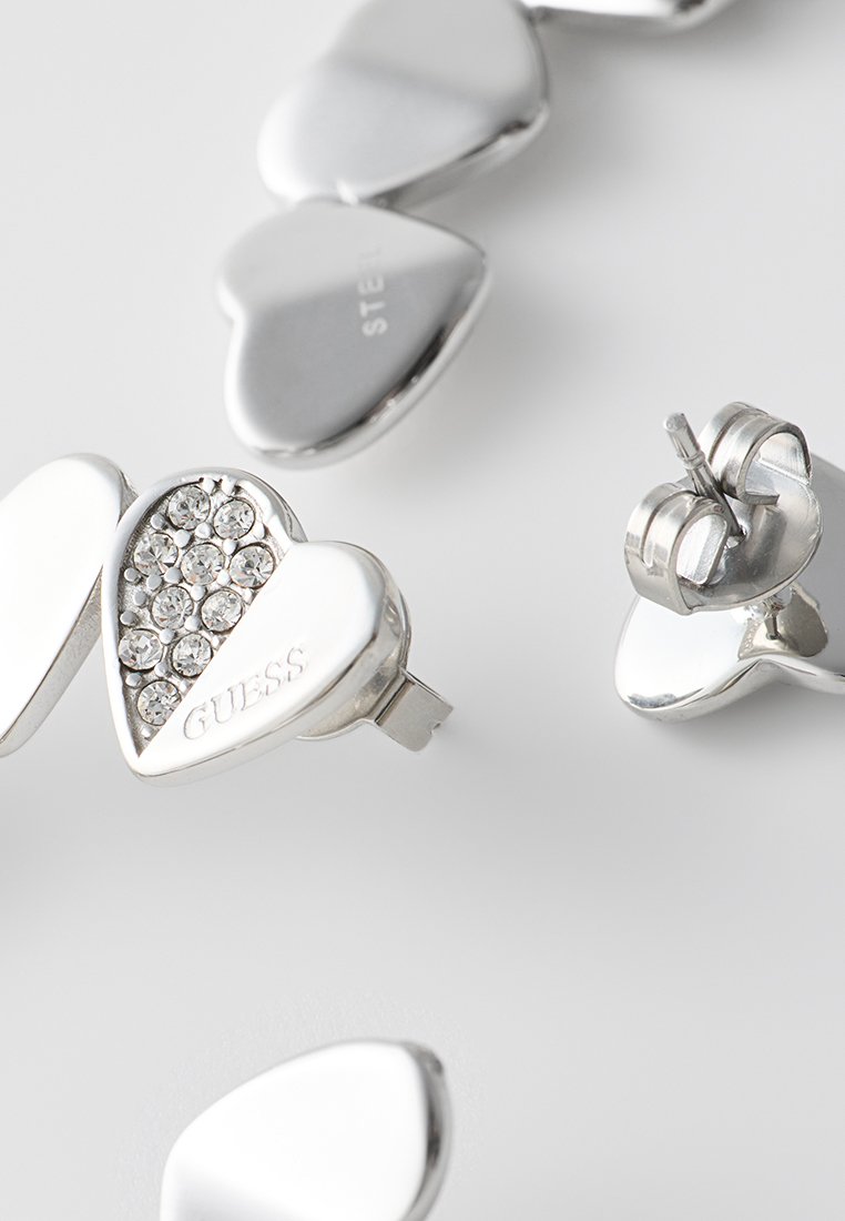 Pendientes de plata en forma de corazón con una superficie texturizada y acentos de cristal, con un nombre de marca prominente en un pendiente.