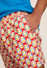 Zwemshorts met een elastische tailleband, met een levendig geometrisch patroon van rood, geel en blauw op een witte achtergrond.