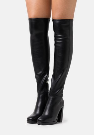 Bottes en cuir noir qui montent au-dessus du genou, avec talons carrés, fermeture éclair latérale et finition lisse et brillante.