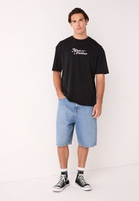 Črna bombažna majica s potiskom "Pink Panther". Svetlo modri jeans kratke hlače, čevlji črni z visokim robom in bele kratke nogavice.