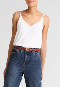 Vit ärmlös topp med v-ringning, parat med högmidjade blå jeans och ett flätat brunt bälte.