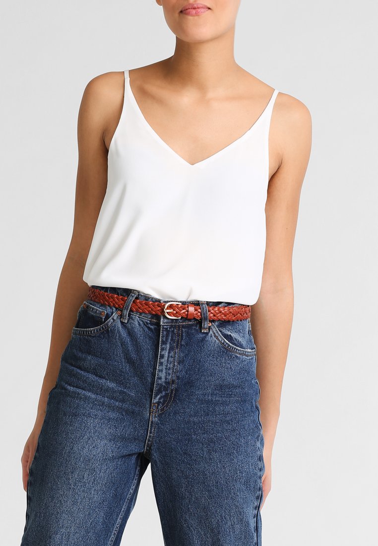 Vit ärmlös topp med v-ringning, parat med högmidjade blå jeans och ett flätat brunt bälte.