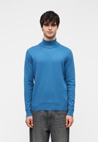 Μπλε πουλόβερ με ζιβάγκο, ελαφρύ πλεκτό υλικό, μακριά μανίκια, ριμπ μανσέτες και τελείωμα, ομαλή υφή, φορεμένο με σκούρο τζιν.