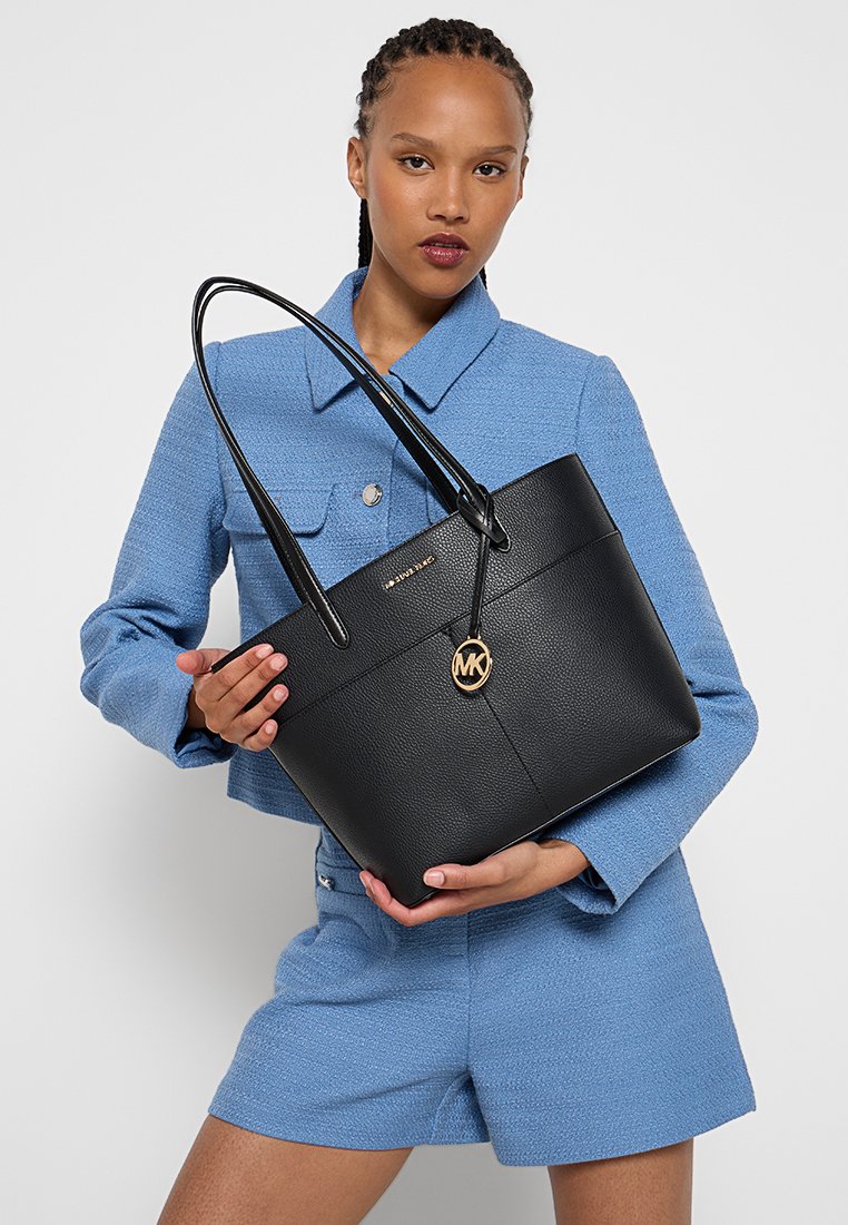 Zwarte leren tote bag met een gestructureerde vorm, voorzien van een gouden logoaccent, dubbele handgrepen en een textuur oppervlak.