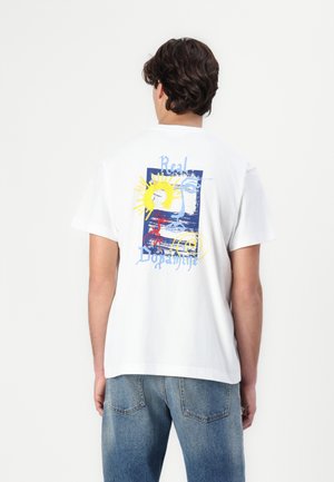 White cotton T-shirt with short sleeves featuring colorful graphic design on the back, including sun, waves, and the text “Real Dopamine.”