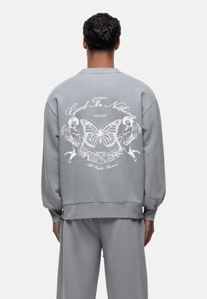 Grijs sweatshirt met lange mouwen en ronde halslijn. Heeft een witte grafische print van een vlinder en figuren op de achterkant, met ribbels aan de manchetten en onderrand.