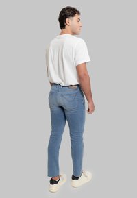 Jeans slim fit azzurri chiaro con sfumature delicate, cinque tasche e una patch con logo sulla cintura posteriore, abbinati a una t-shirt bianca e sneakers.