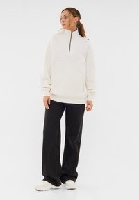 White fleece quarter-zip pullover with a high collar, front pocket, and ribbed cuffs, paired with black wide-leg pants and beige sneakers.