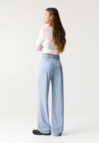 Hellblaue weit geschnittene Hosen mit glatter Textur, ausgestattet mit einem taillierten Bund und unsichtbaren Seitentaschen, kombiniert mit einem weißen Langarmoberteil.