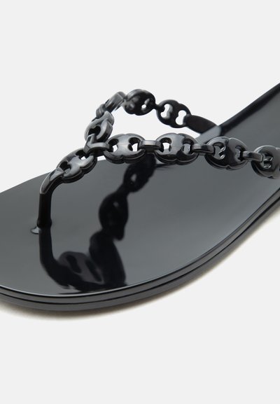 Γυαλιστερό μαύρο σανδάλι με διακοσμητικό λουράκι με αλυσίδα στην περιοχή των δακτύλων σε ουδέτερο φόντο.