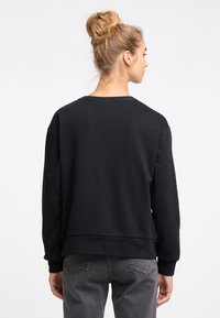 Hanorac negru, cu o croială lejeră, guler rotund și mâneci lungi. Fabricat dintr-un material neted, cu un design cu umeri lăsați.