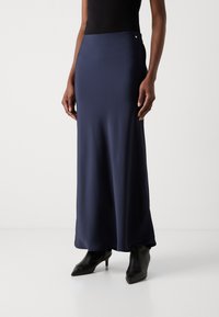 Navy satiini maxi-hame, jossa on sileä pinta, korkea vyötärö ja koristeellinen hopeinen yksityiskohta vyötärön ympärillä, yhdistettynä mustiin teräväkärkisiin nilkkasaappaisiin.