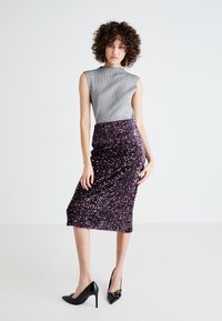 Hopeapintainen hihaton paita, jossa on ribbitekstuuri, yhdistettynä slim fit -violettiin glitter-midi-hameeseen. Mustat kärjet korkokengät täydentävät asua.
