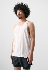 Vit ärmlös linne med perforerat mönster, med en lös passform och en liten röd logotyp på nedersta vänstra delen, tillsammans med svarta shorts.