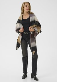 Striped shawl made of soft fabric in shades of brown, cream, and gray, featuring a geometric pattern and fringed edges. Black outfit underneath.