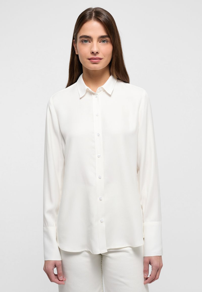 Witte blouse gemaakt van gladde, lichte stof. Heeft een klassieke kraag en lange mouwen met knoopmanchetten.