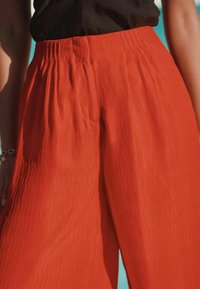 Pantalons larges rouges en tissu léger, avec une finition texturée et une taille élastique, ornés de plis pour un détail supplémentaire.