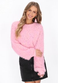 Różowy puszysty sweter z kolorowymi spryskaniami, okrągłym dekoltem i szerokimi rękawami, zestawiony z ciemnoniebieską spódnicą z denimu. Miękka tekstura i luźny krój.