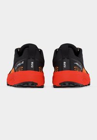 Ζευγάρι μαύρων και πορτοκαλί παπουτσιών τρεξίματος Altra GTR, εμφανιζόμενα από πίσω, με υφασμένη φωτεινή πορτοκαλί σόλα και θηλιές στο πίσω μέρος της φτέρνας.