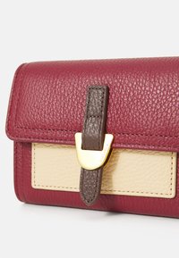 Leather wallet with a textured burgundy finish, cream accent panel, and a dark brown strap. Features gold-tone hardware for closure.