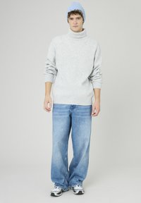 Pull à col roulé gris clair avec une texture côtelée, associé à un jean bleu clair à coupe décontractée. Les accessoires comprennent un bonnet tricoté bleu doux.