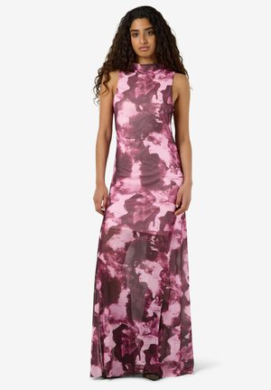 Femme aux longs cheveux bouclés portant une robe sans manches, à col haut, longue jusqu'au sol, rose et violette à motif abstrait.
