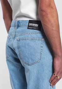 Jeans in denim azzurro chiaro con vita alta, dotati di due tasche posteriori, cuciture a vista e un'etichetta nera del marchio sulla vita.