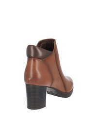 Botas de tobillo de cuero marrón con puntera redondeada, diseño curvado y tacón apilado. Acentos en marrón oscuro en el tacón y el collar. Acabado suave.