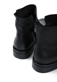 Czarne skórzane botki za kostkę o gładkiej teksturze, z niskim obcasem, zamkiem błyskawicznym po boku oraz otwartym tyłem.