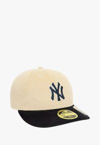 Gorra de béisbol de pana beige con visera negra. Presenta un logo bordado de los New York Yankees en azul y una etiqueta amarilla de tamaño en el borde de la visera.