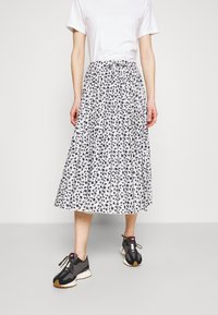 Jupe midi plissée florale noir et blanc avec une taille cintrée, associée à des baskets noir et gris. Tissu lisse avec une texture aérienne.