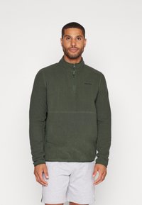 Giacca in pile verde con design a mezzo zip, caratterizzata da un colletto alto e un discreto dettaglio del logo sul petto. Morbida al tatto e con vestibilità casual.
