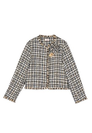 Giacca in tweed a quadri neri, bianchi e beige con maniche lunghe, bordi sfrangiati e due fiori decorativi in tessuto sul petto.