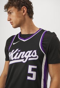 Juodas krepšinio marškinėliai su violetiniais akcentais, su užrašu "Kings" baltos spalvos, numeriu 5 ir V formos iškirpte. Medžiaga atrodo kvėpuojanti.