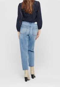 Světle modré džíny s vysokým pasem a rovným střihem. Zadní část obsahuje dvě našité kapsy a viditelné švy. Nosit s béžovými kotníkovými botami.