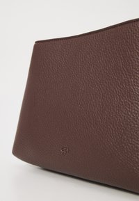 Borsa a mano in pelle marrone con superficie texture, caratterizzata da un logo in rilievo discreto e una forma strutturata.