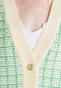 Pletený cardigan s vzorem zeleno-krémových kostek, se zlatým knoflíkem na výstřihu a designem límce ve tvaru V.
